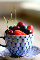 Vintage porcelain cup filled with strawberries, blueberries and cherries. Selective focus. 