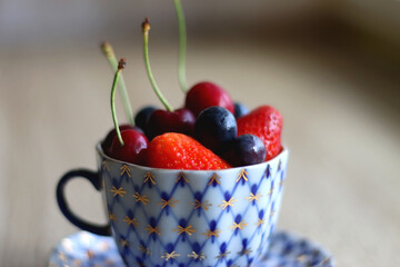 Vintage porcelain cup filled with strawberries, blueberries and cherries. Selective focus. 