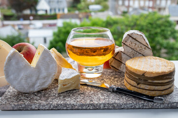 Cow cheeses of Normandy - camembert, livarot, neufchatel, pont l'eveque and glass of apple cider drink with houses of Etretat village on background, Normandy, France - obrazy, fototapety, plakaty