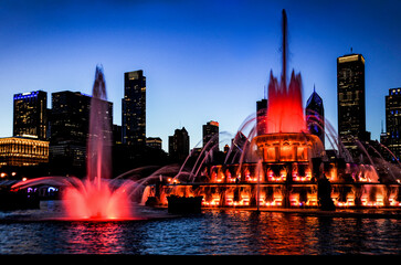 Fototapeta premium Buckingham Water fountain in red as the twilight sky turns purple silhouetting the Chicago city skyline.