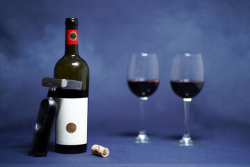 Opened dry, red wine and an exclusive corkscrew with a cork including two wine glasses. (Whole picture with smoke and grey background)  