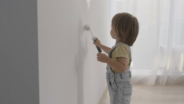 Little baby child standing and painting the white wall, funny boy care of home