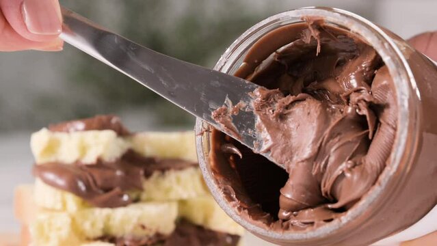 Chocolate spread on a knife and sweet toast for breakfast, favorite children's food. Closeup texture of pasta and gooey chocolate mixture. Place for text, ideal for advertising. Copy space 