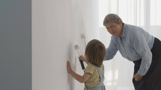 Grandmother learning little child to paint white wall, family love portrait, teamwork, different generation work together, gap over generation