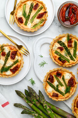 Tartlets or quiches with asparagus, sun-dried tomatoes and feta cheese on plates. Top view