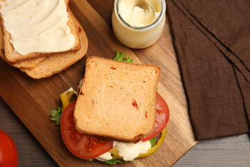 Delicious sandwich with vegetables and mayonnaise served on wooden table, flat lay