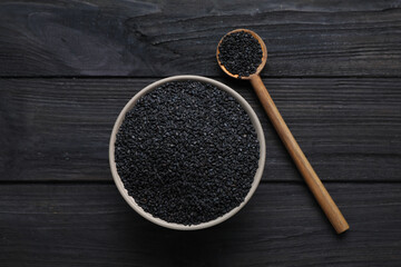 Bowl and spoon with black sesame seeds on wooden table, flat lay