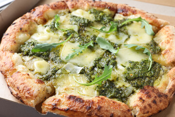 Delicious pizza with pesto, cheese and arugula in cardboard box, closeup