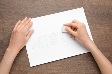 Obraz premium Woman erasing word on sheet of white paper at wooden table, top view