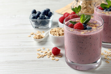 Tasty smoothie with berries, mint and oatmeal on white wooden table, space for text