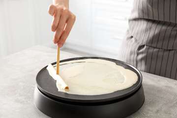 Woman cooking delicious crepe on electric pancake maker at table indoors, closeup