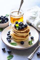 Pancakes stack with fresh blueberries and honey at white stone table.