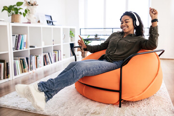 Excited black lady listening to music in headphones and dancing