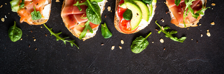 Open sandwiches set with cream cheese, prosciutto, salmon, avocado and fresh greens and vegetables....