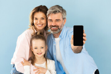 Happy Family Showing Cellphone With Empty Screen On Blue Background