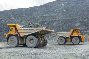 Obraz na płótnie Canvas Transportation of copper ore rocks by dump trucks. Large quarry yellow truck. The mining truck drives through the quarry.