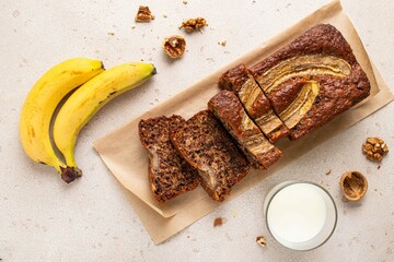Traditional American homemade sliced banana bread with chopped walnuts, chocolate chips and cinnamon and milk on light background. Fruit cake. Pound cake. Breakfast background.