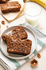 Pieces of american homemade sliced banana bread with chopped walnuts, chocolate chips and cinnamon on light background. Breakfast concept with milk. Vegan healthy food. Selective focus.