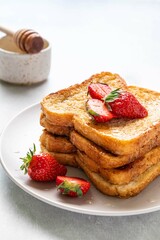 Stack of french toast covered with strawberries and honey on light background. Morning breakfast, brunch or lunch concept. Selective focus.