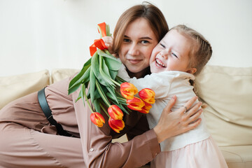 Postcard for March 8. Little daughter kisses and hugs mother with yellow flowers, tulips. Mothers Day