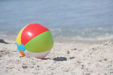 Obraz premium Multi colored beach ball on a sandy beach near the ocean in horizontal format