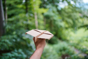Man holding a brown paper plane in the fresh air in the forest, closeup. Space for text.	