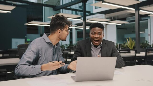 Happy male partners diverse businesspeople arabian african colleagues look at laptop rejoice good news commercial offer excited millennial men give five win online lottery feeling triumph shake hands 
