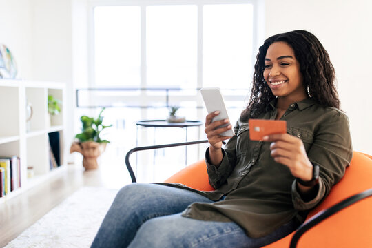 Smiling black lady using phone and credit card at home