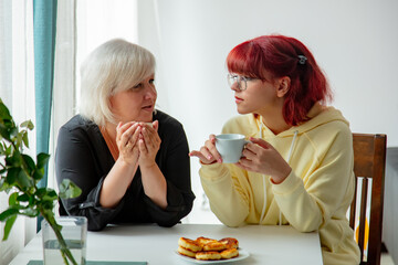 Mother with teen daughter sit at table and drink coffee with cheesecakes