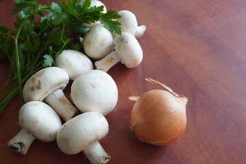 White champignon mushrooms, onion and parsley green leaves on wooden table

