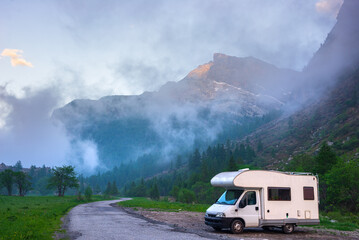 Camper van in the mountains, the Alps, Piedmont, Italy. Sunset dramatic sky and clouds, unique highlands and rocky mountains landscape, alternative vanlife vacation concept.