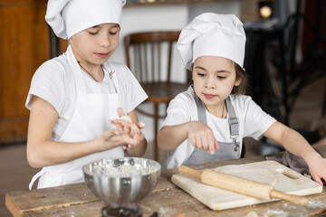 Brother and sister baking homemade sweet pie together, having fun. Home bakery, little kids in process of food preparation in the kitchen at home, helping mother, doing chores