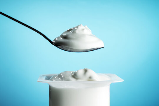 White plastic pot with yogurt and spoon on blue background