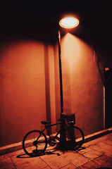A bicycle left under a street lamp at night.