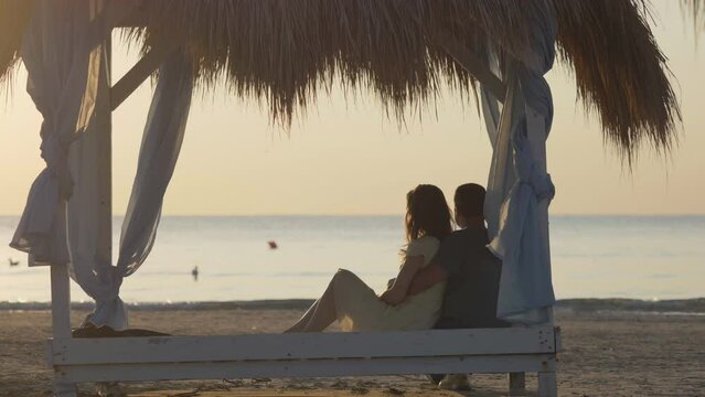 Man hug woman and sit together in canopy, romantic couple admire serene sea, sky