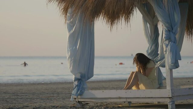 Sad woman with face in hands sit in canopy, girl crying, peaceful sea
