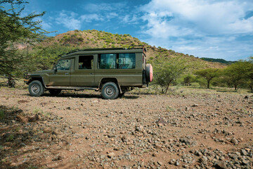 Obraz na płótnie Canvas A safari vehicle in the wild against the background of Shompole Hills in Kajiado, Kenya