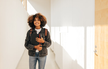 Beautiful female student walking through college hallway. Girl going for the class and smiling.