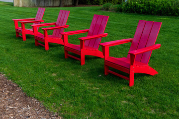 Row of red Adirondack chairs at lake shore on a grassy lawn
