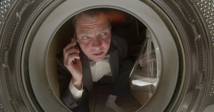 Portrait in the washing machine. A man in a suit calls a repair service on the phone. Reporting a breakdown of an electronic device. He opens the glass door with his hand.