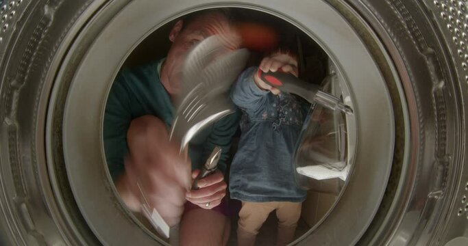 Cheerful young father and daughter are repairing a washing machine. He expressively shows the tools, looks into the camera. The girl is using a screwdriver.