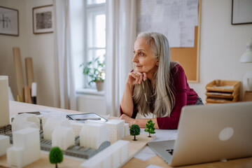 Senior woman eco architect with model of modern bulidings working in office.