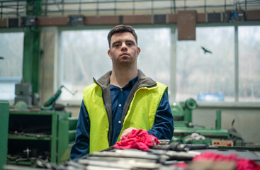 Young man with Down syndrome looking at blueprints when working in industrial factory, social...