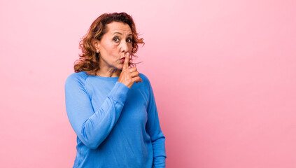 middle age hispanic woman asking for silence and quiet, gesturing with finger in front of mouth,...
