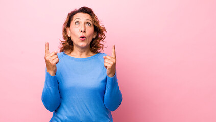Fototapeta middle age hispanic woman feeling awed and open mouthed pointing upwards with a shocked and surprised look obraz