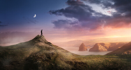 A man walking stands high on a hillside watching as the sunsets on a coastline landscape. Freedom...