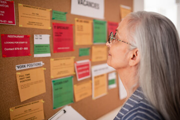 Job center employee with file form standing in front of employment noticeboard.
