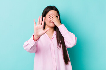 young adult woman covering face with hand and putting other hand up front to stop camera, refusing...