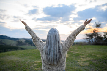 Rear view of senior woman with arms outstretched and face up at park on spring day