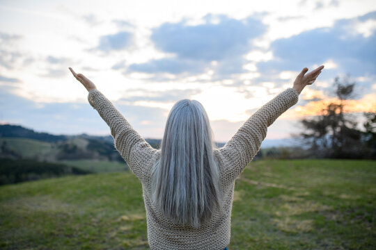 Rear View Of Senior Woman With Arms Outstretched And Face Up At Park On Spring Day